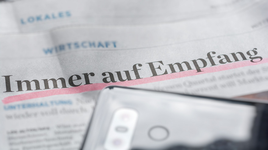 Nahaufnahme eines Mobiltelefons mit Zeitung im Hintergrund