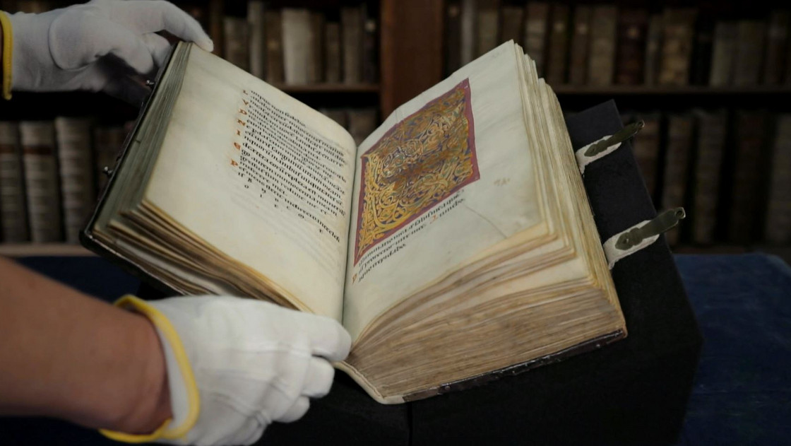 Eine Person blättert mit sterilen Handschuhen ein altes Buch auf.