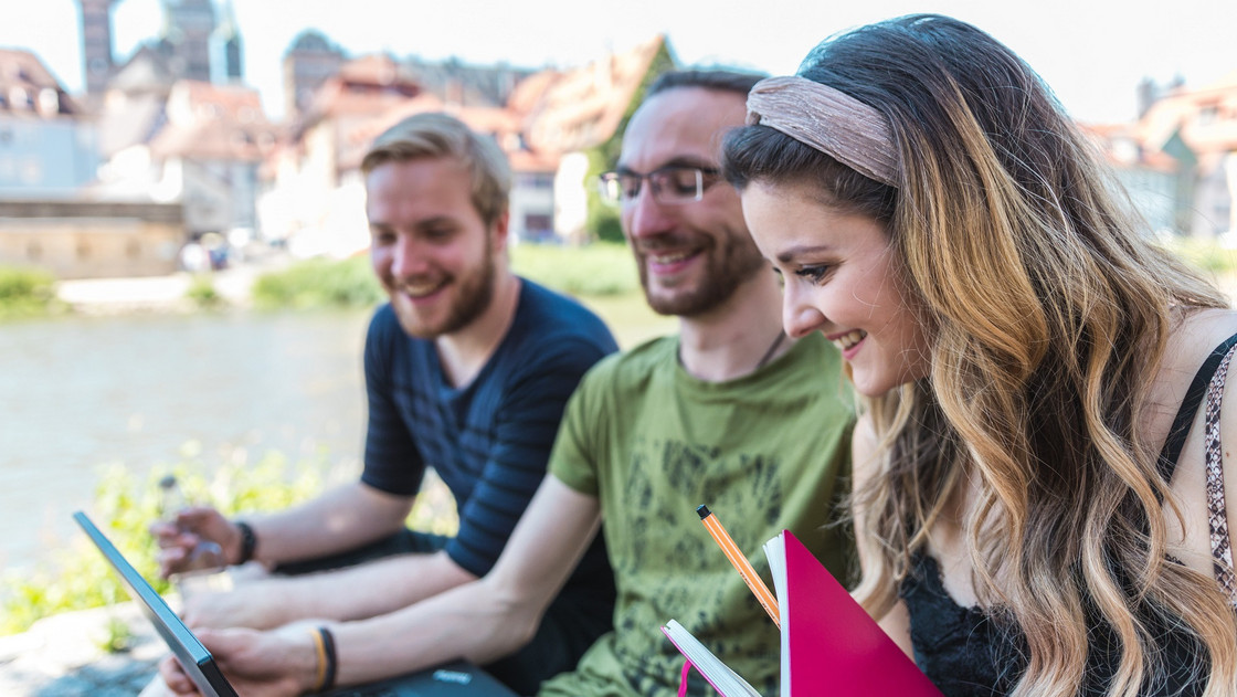 Drei Studierende sitzen in Klein-Venedig und schauen auf einen Laptop.