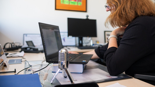 Ute Schmid sitzt am Schreibtisch mit Mikro und Laptop