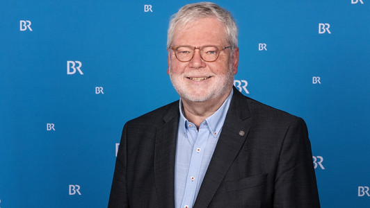 Der ehemalige Bamberger Universitätspräsident Godehard Ruppert steht vor einem Banner mit dem Logo des Bayerischen Rundfunks.