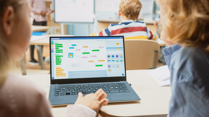 Zwei Kinder sitzen am Laptop und surfen im Internet.