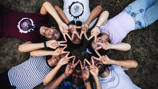 Sechs Studierende liegen auf dem Boden und zeigen mit ihren Fingern das Symbol für Frieden.