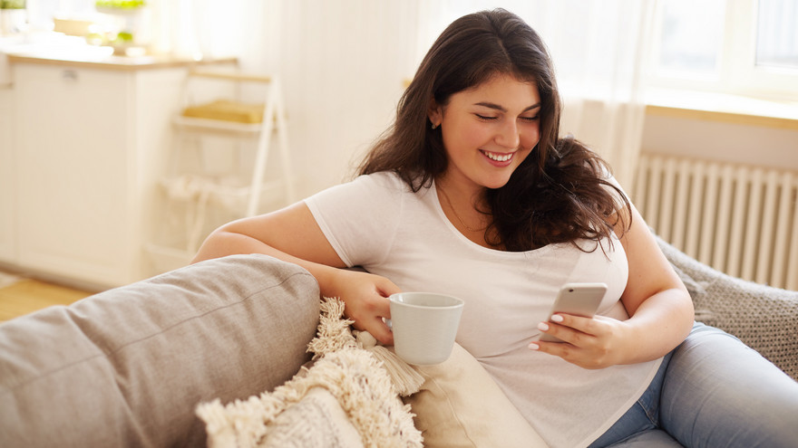 Frau sitzt auf dem Sofa und bedient ihr Handy.