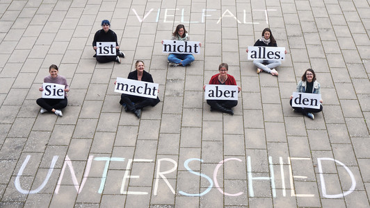 Frauen sitzen auf dem Boden auf dem Uni-Erba-Gelände und zeigen das auf Schildern notierte Statement: "Vielfalt ist nicht alles. Sie macht aber den Unterschied."