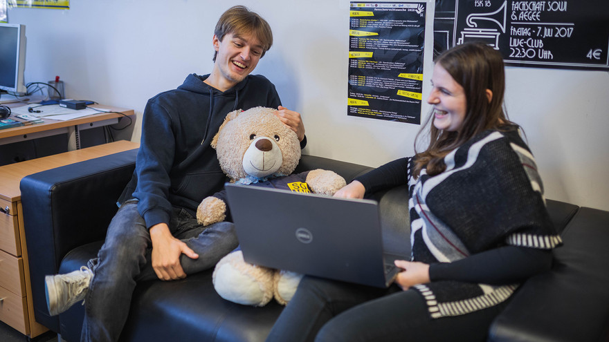 Linus und Valentina sitzen lachend auf der Coach im Fachschaftszimmer