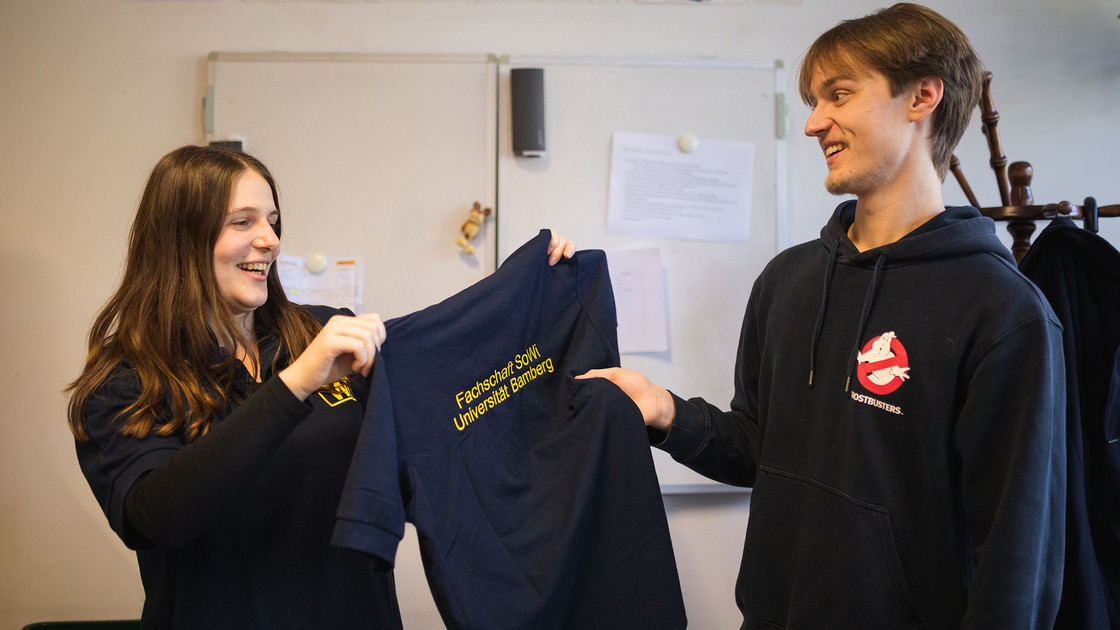 Fachschaftssprecher*innen Valentina und Linus mit Merchandising im Fachschaftszimmer